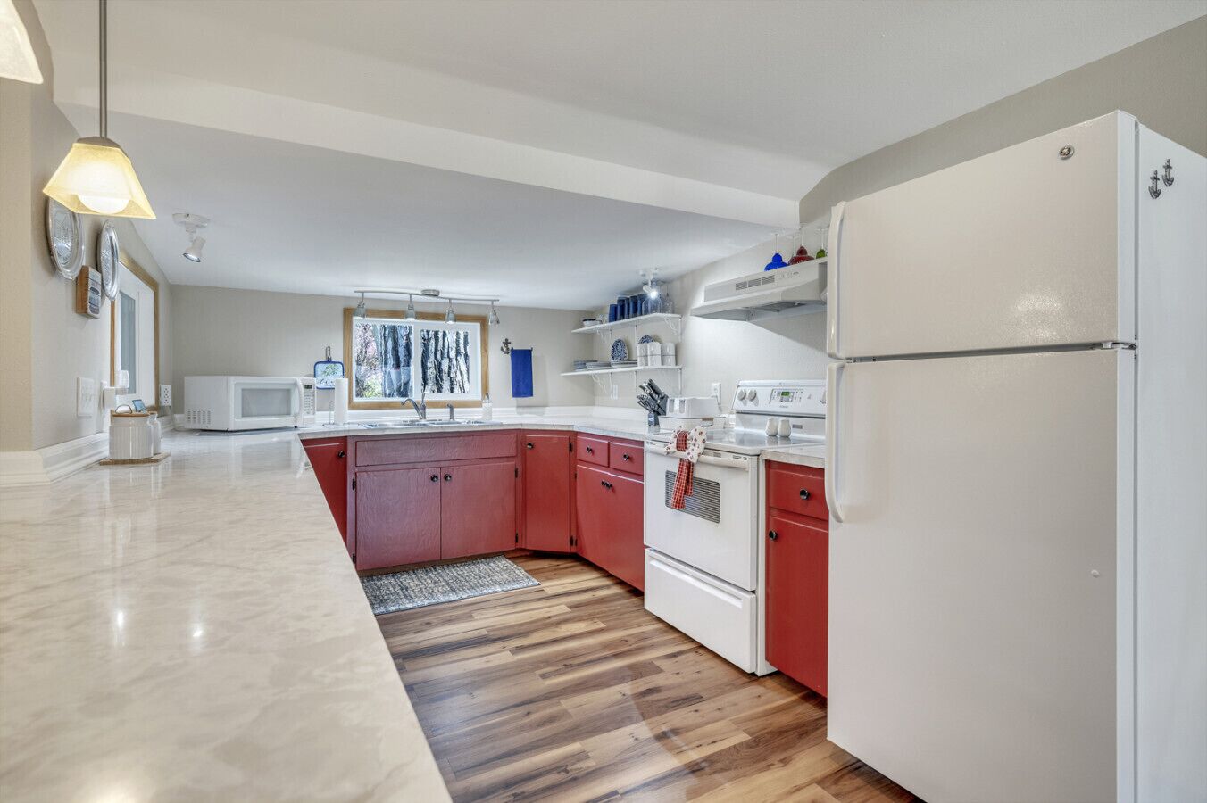 A modern kitchen with a white refrigerator, red cabinets, a microwave, and a window with a view of trees.