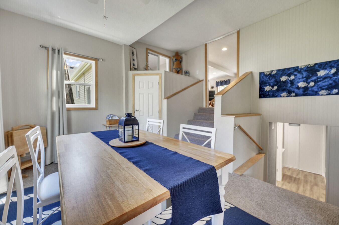 Un espace repas avec une table en bois, des chaises, une lanterne et un escalier menant à un autre niveau.
