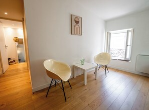 Ein Zimmer mit zwei Sesseln, einem kleinen Tisch, einem gerahmten Bild an der Wand und einem Fenster mit Aussicht.