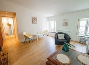 Ein geräumiger Wohnbereich mit Holzboden, einem grauen Sessel, einem weißen Tisch und zwei weißen Stühlen.