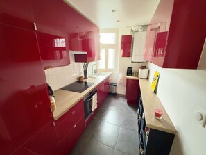 A modern kitchen with red cabinets, a black countertop, and a small sink. - Beautiful T2 in the 17th arrondissement (Paris)