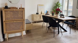 Ein Essbereich mit einem Holztisch, schwarzen Stühlen, einem Rattankorpus und einem großen Fenster mit Blick auf Gebäude.