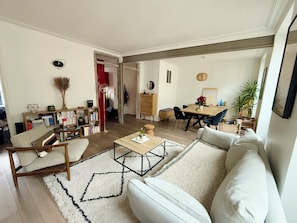 A spacious living area with a sofa, coffee table, bookshelf, and dining table. - Beautiful T2 in the 17th arrondissement (Paris)