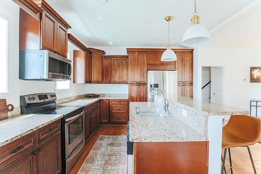 A kitchen with wooden cabinets, stainless steel appliances, a granite countertop, and a hanging light fixture.