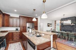 A kitchen with granite countertops, wooden cabinets, stainless steel appliances, and pendant lighting. - Luxury Stay w/ Fenced Yard, Hot Tub, Mountain View (Afton)
