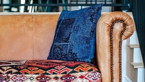 A brown leather sofa with a patterned cushion and a blue pillow, positioned in a room with a staircase and a neon sign in the background. - Luxury Stay w/ Fenced Yard, Hot Tub, Mountain View (Afton)