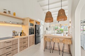 Eine moderne Küche mit Holzausstattung, einem schwarzen Kühlschrank und einer Bar mit Korbstühlen.
