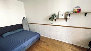 A bedroom with a bed, a shelf with books and a plant, and a wall with a patterned design. - Cocoon with garden in Bordeaux (Bordeaux)
