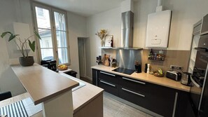 A modern kitchen with a central island, stainless steel appliances, and a window with a view. - Cocoon with garden in Bordeaux (Bordeaux)