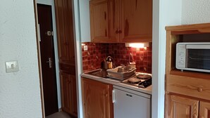 Una cocina pequeña con armarios de madera, un microondas integrado y un escurreplatos.