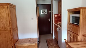 Un pasillo estrecho con armarios de madera, un microondas y una puerta que da a otra habitación.