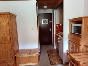 A narrow hallway with wooden cabinets, a microwave, and a door leading to another room. - Studio Granon view, near slopes (Saint-Chaffrey)