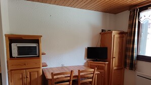 Una habitación pequeña con una mesa de madera, sillas, un televisor y un armario.