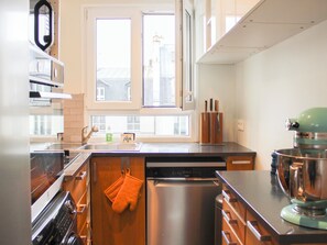 A modern kitchen with stainless steel appliances, wooden cabinetry, and a window with a view of buildings. - 96m² flat, overlooking Paris rooftops (Paris)