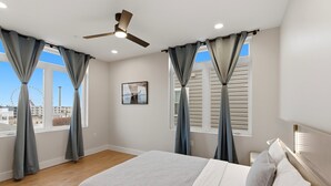 Une chambre à coucher avec un lit, un ventilateur de plafond et des fenêtres avec des rideaux.