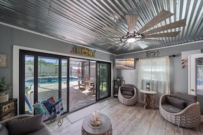 A spacious room with a large sliding glass door leading to an outdoor area, a ceiling fan, wicker chairs, and a small round table.