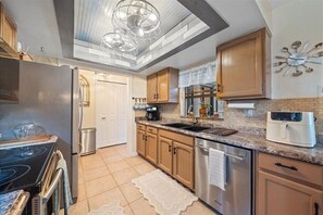 A modern kitchen with a built-in oven, stainless steel appliances, wooden cabinets, and a unique ceiling light fixture.