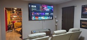 Ein Zimmer mit einem großen Flachbildfernseher, der eine Star Trek-Serie zeigt, einem Bücherregal, einer Couch und einem Massagesessel.