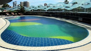 A swimming pool with a wavy glass barrier, a tiled deck, and a city skyline in the background. - Hilton Durban (Durban)