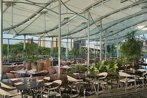 Un restaurant en plein air avec des tables et des chaises, un plafond en verre et des plantes en pot.