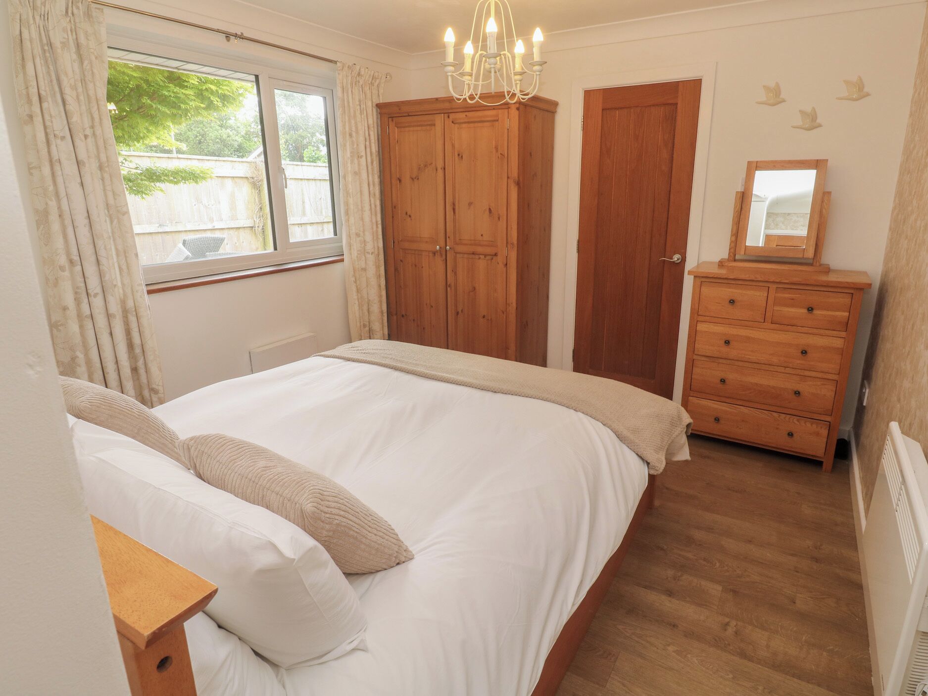 Quarto com cama, guarda-roupa de madeira, cômoda e janela com cortinas.