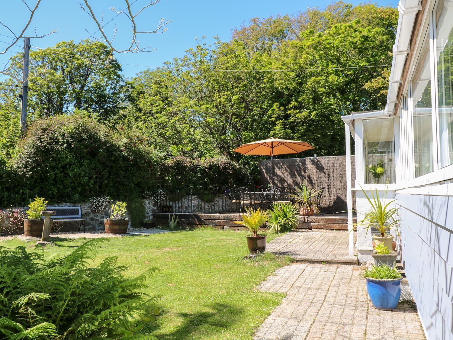 Um jardim com um pátio pavimentado, móveis de exterior e plantas em vasos.