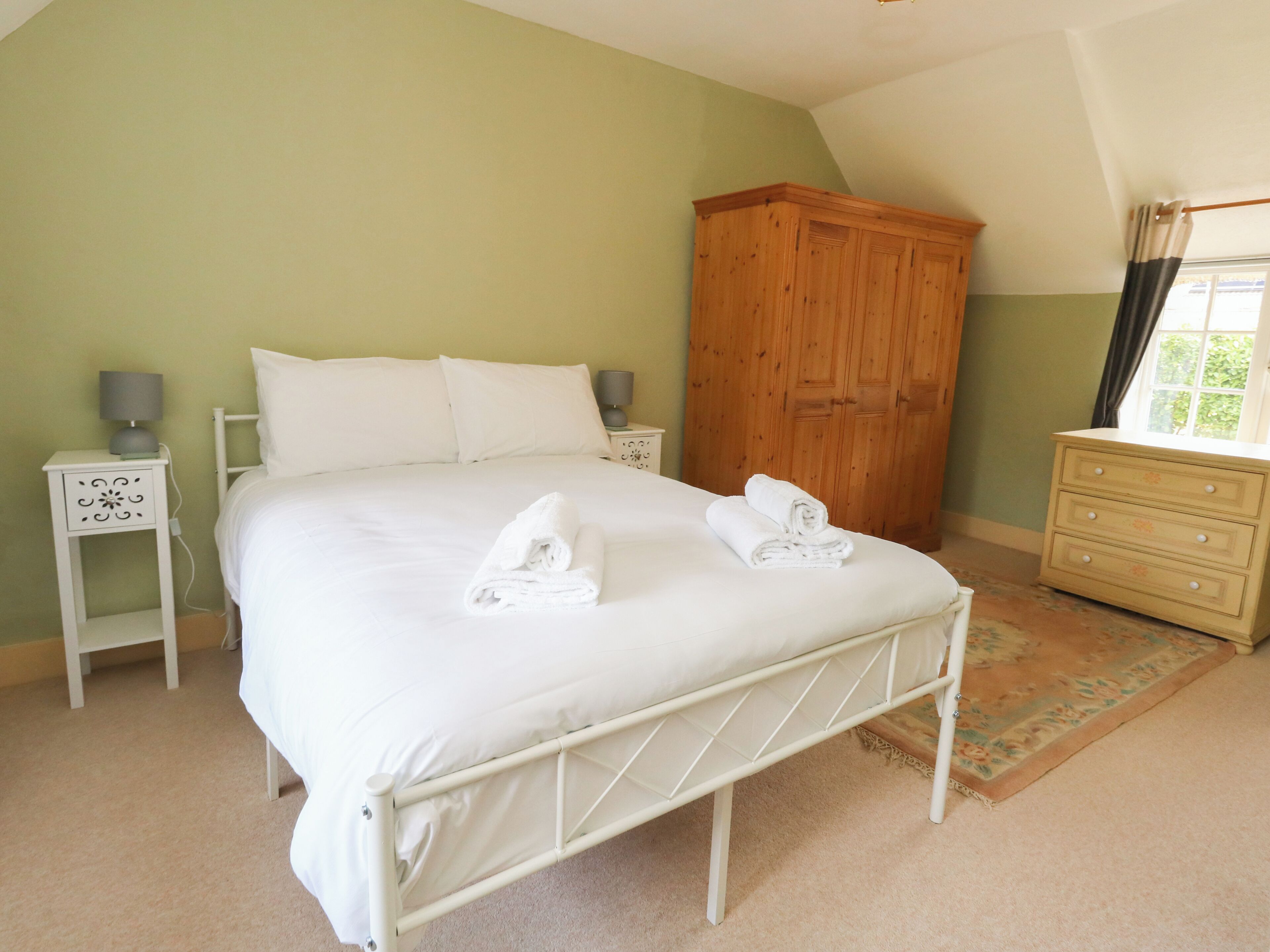 A bedroom with a bed, two bedside tables, a wooden wardrobe, and a window with curtains.
