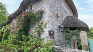 Een stenen cottage met rieten dak, een bordje met de tekst 'Rose Cottage' en een lantaarn aan de muur.