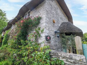 A stone cottage with a thatched roof, a sign reading 'Rose Cottage,' and a lantern on the wall. - Rose Cottage (Weymouth)