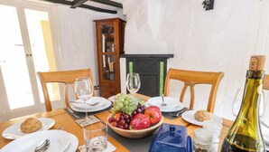 Een eettafel voor vier personen, gedekt met borden, bestek, glazen, een fruitschaal, een fles wijn en een zout- en peperstel.