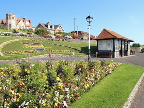 A town square with a flower bed, a building with a red roof, and a sign with 'EVERYBODY' written on it. - Rose Cottage (Weymouth)