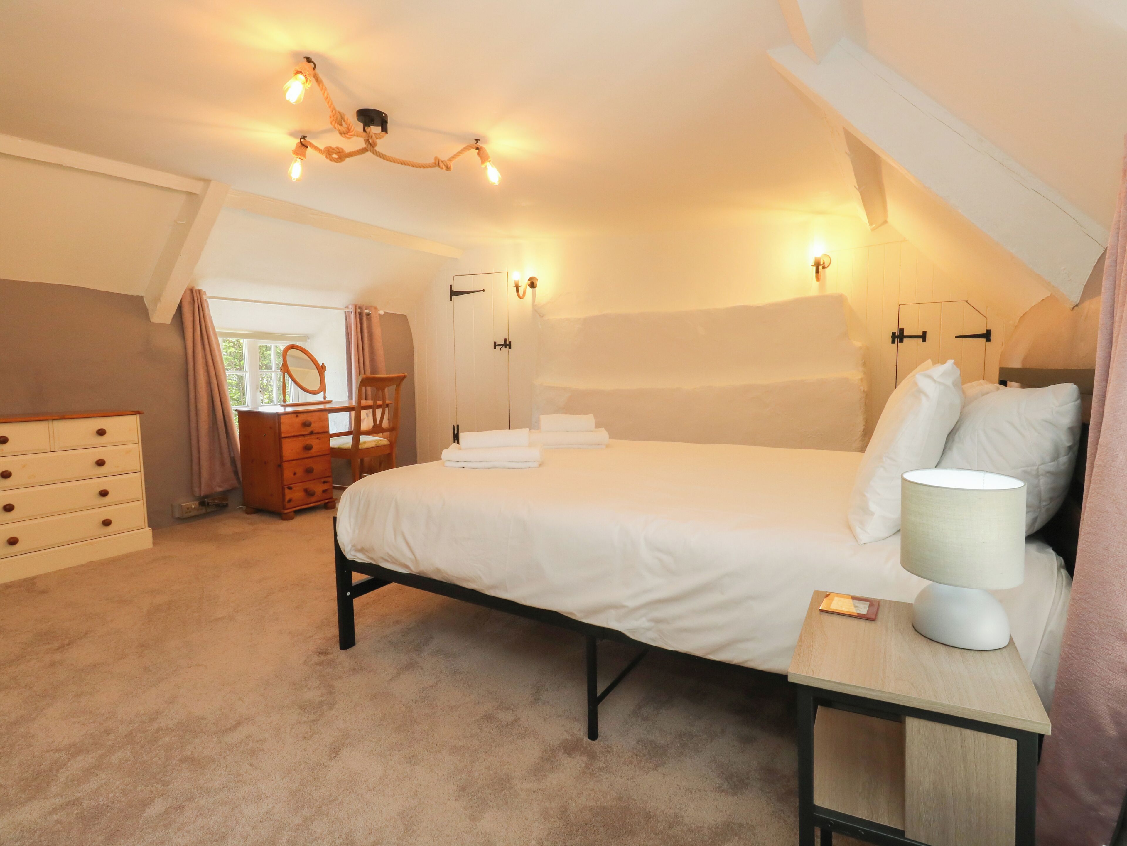A bedroom with a bed, dresser, vanity, and a chandelier.