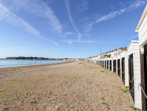 A pebbled beach with a row of white buildings on one side. - Rose Cottage (Weymouth)