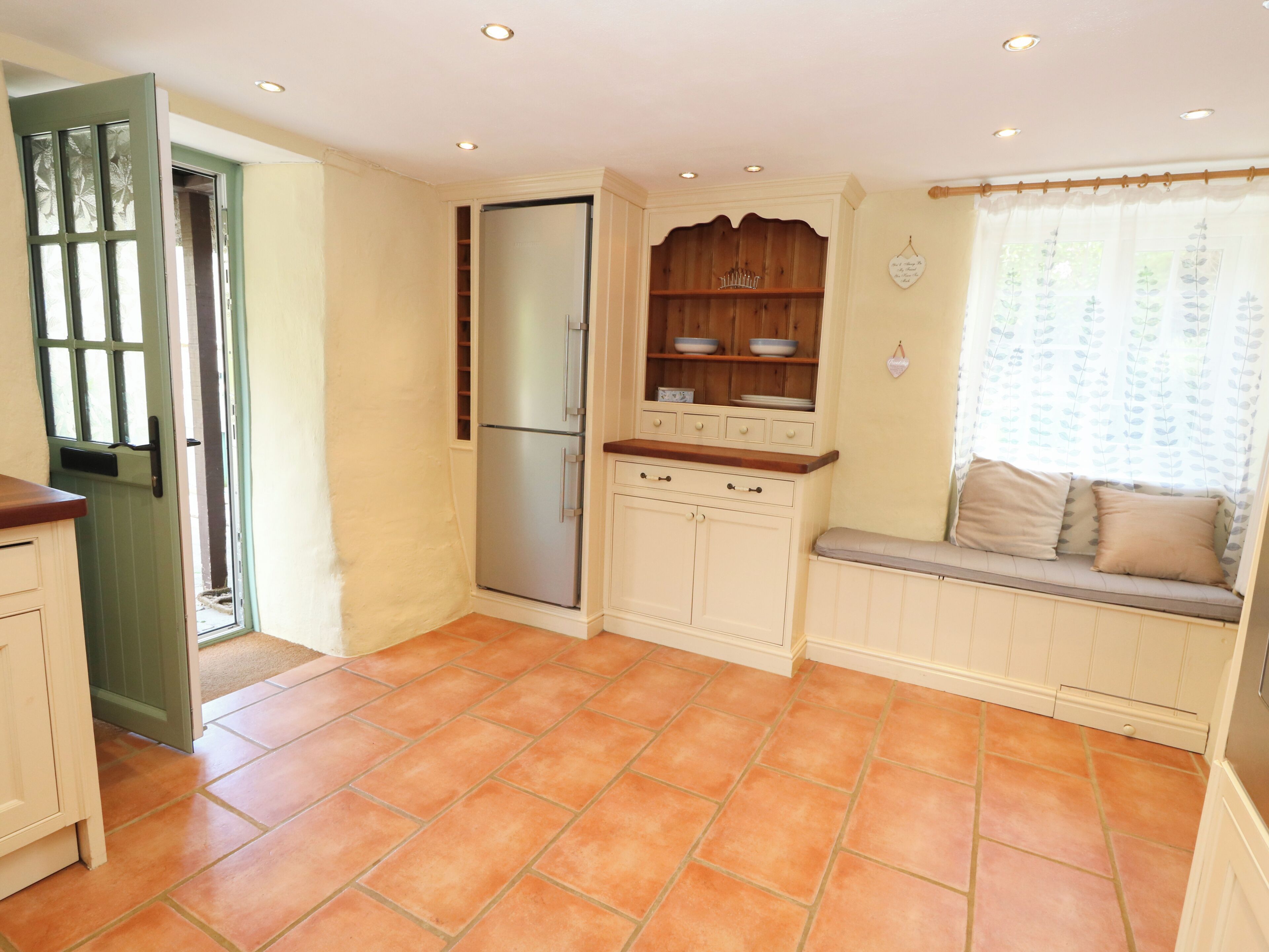 A kitchen with a built-in refrigerator, a window seat with cushions, and a door leading to an outdoor area.