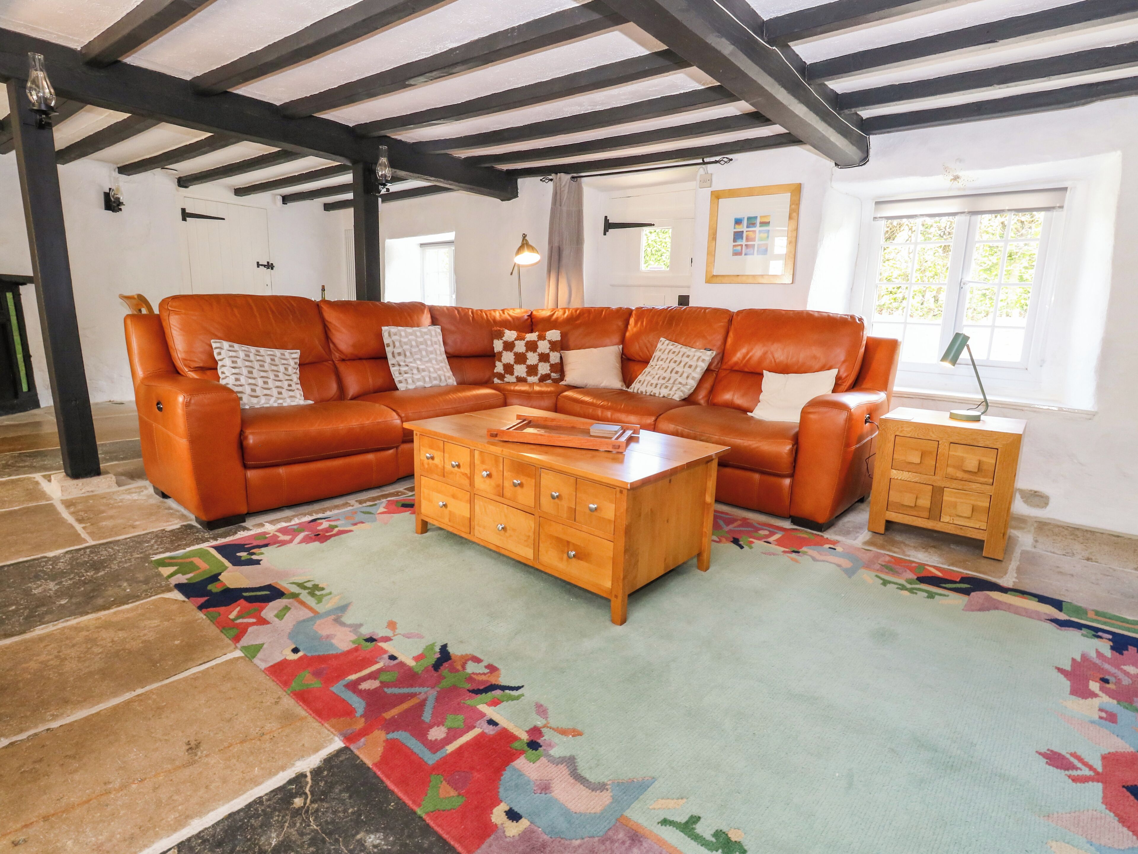 A living room with a sectional sofa, a wooden coffee table, a patterned rug, and a wooden nightstand.