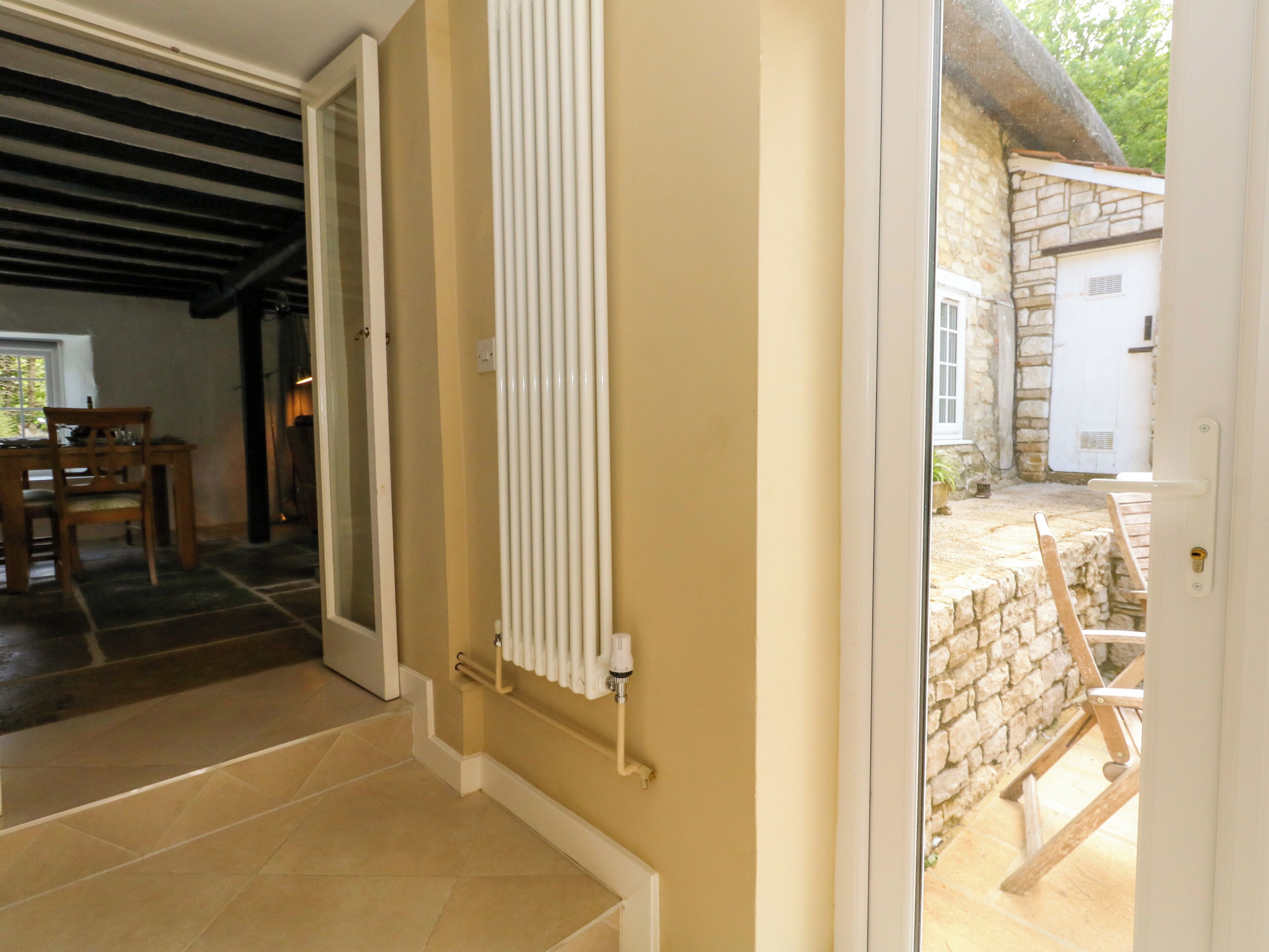 Puerta abierta que da a un comedor con mesa y sillas, un radiador en la pared y un muro de piedra en el exterior.