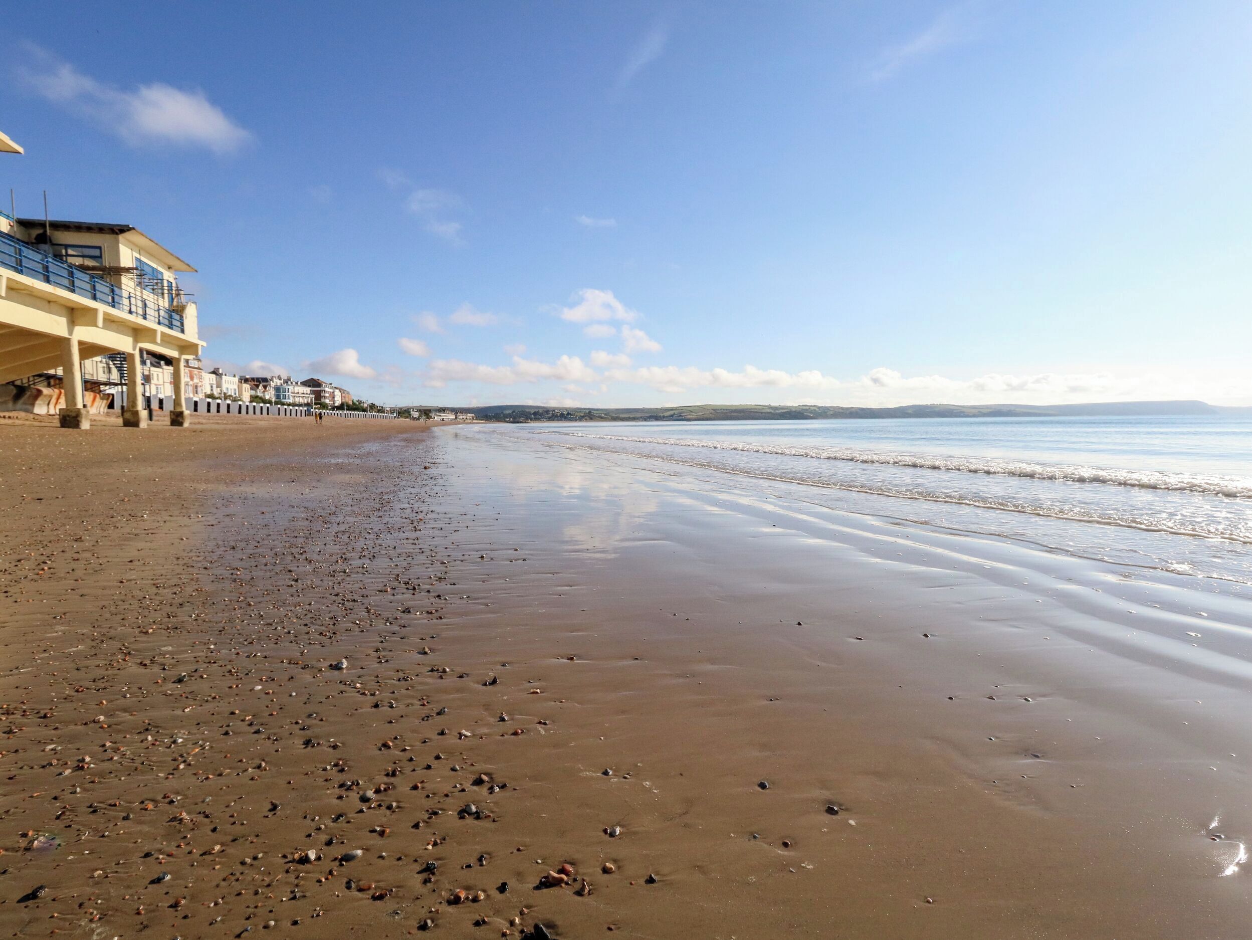 A beach with a building on the left, a clear sky, and calm water.
