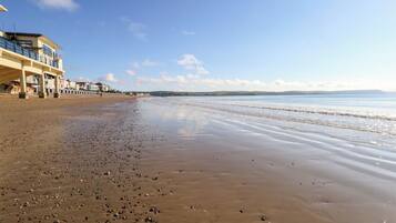 A beach with a building on the left, a clear sky, and calm water.