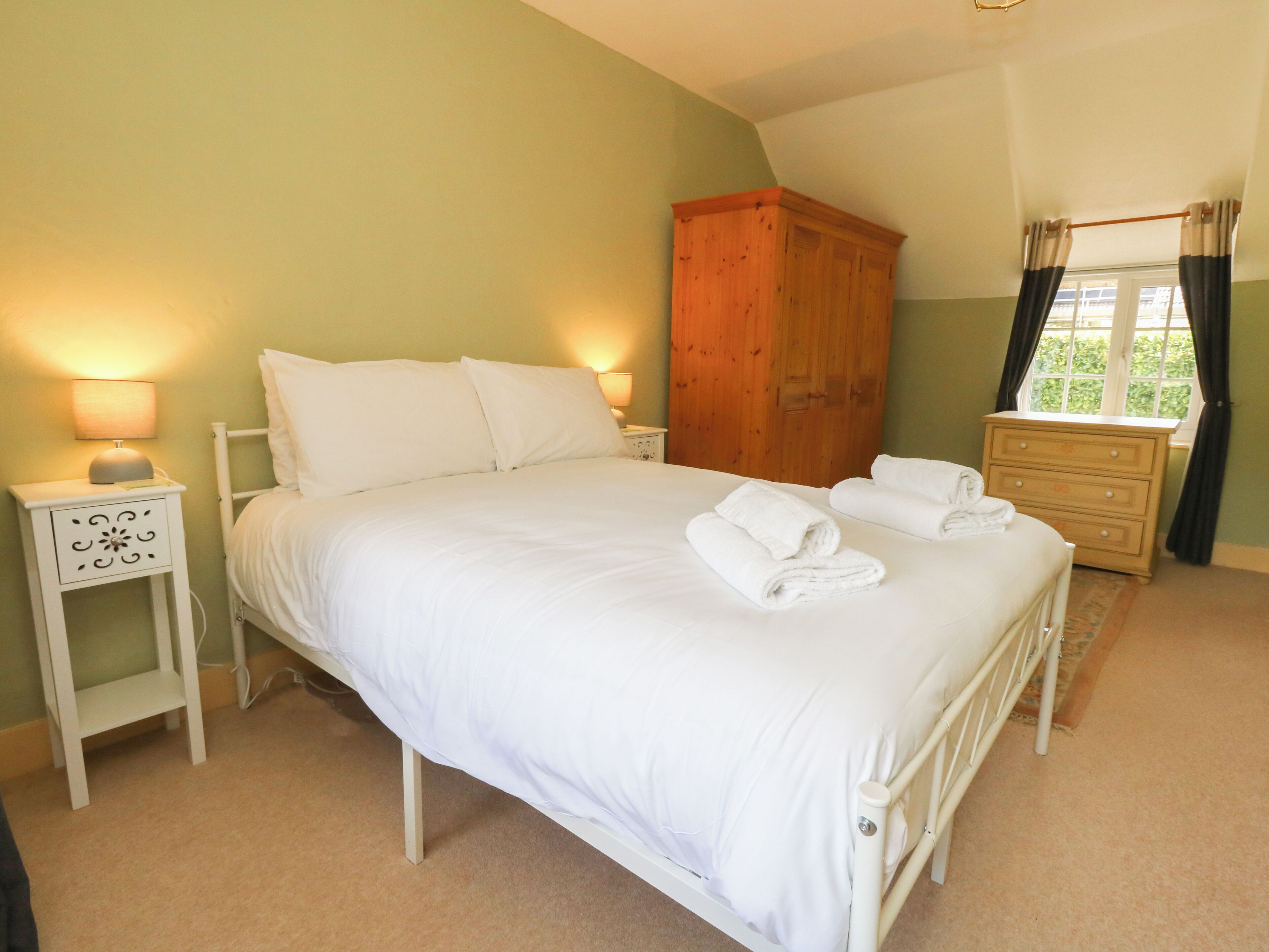 A bedroom with a bed, nightstands, a dresser, and a window with curtains.