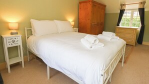 Een slaapkamer met een bed, nachtkastjes, een dressoir en een raam met gordijnen.
