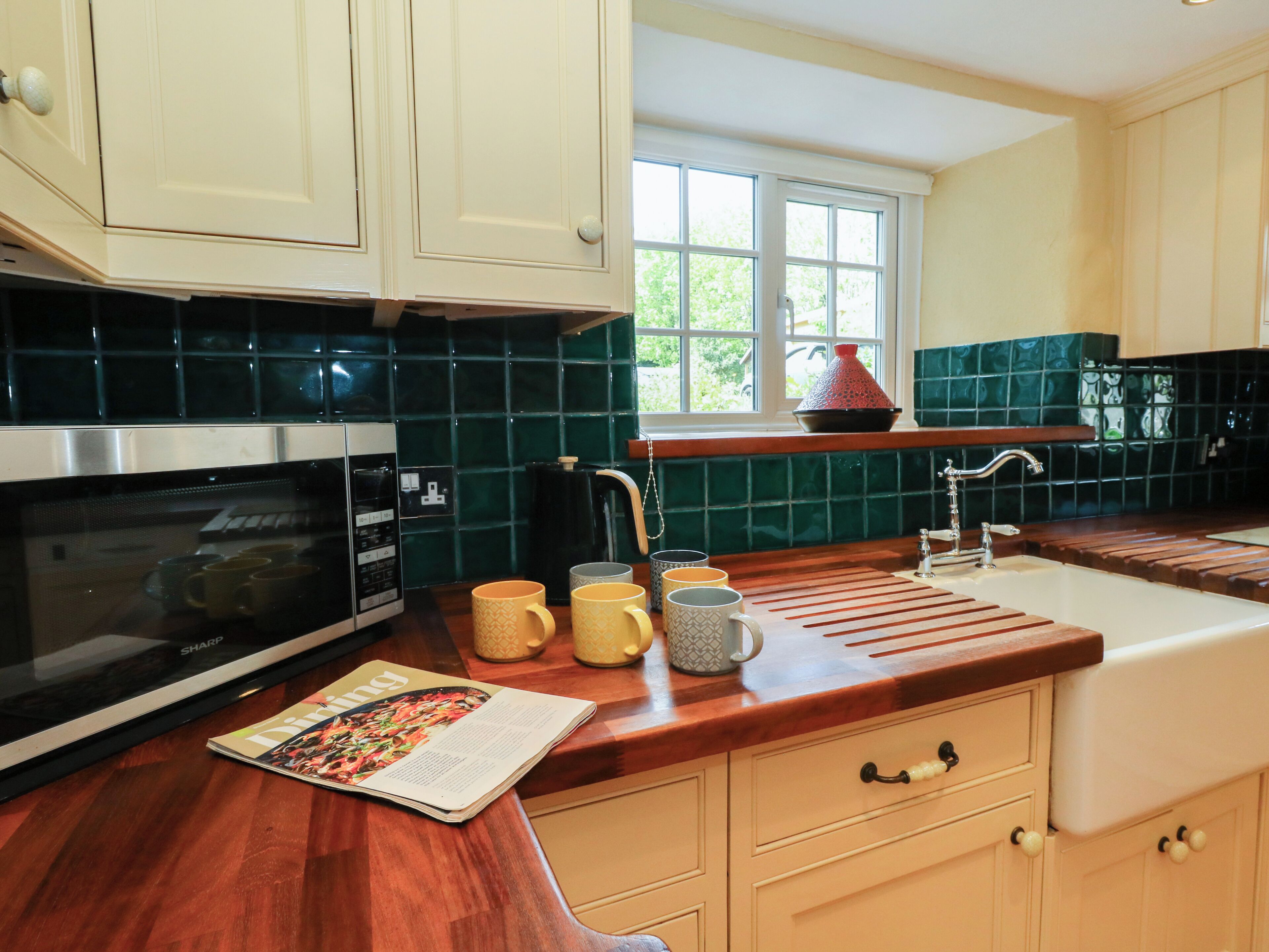 A kitchen with a microwave, a coffee maker, and a window with a view of greenery.