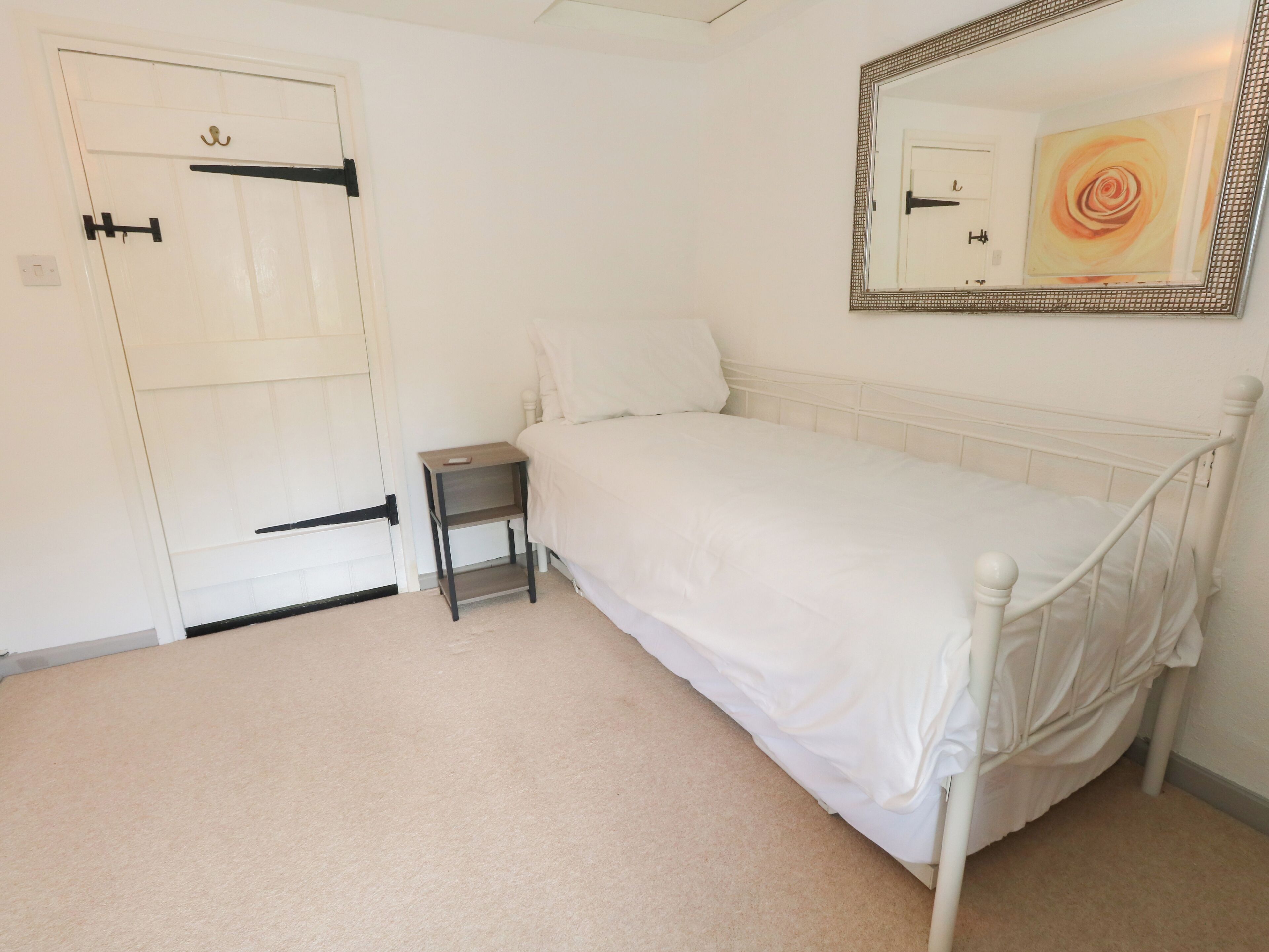 Un dormitorio con una cama individual, una mesita de noche, una puerta con pomo negro y un espejo en la pared.