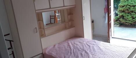 A bedroom with a bed, a wardrobe, and a window with a view of greenery.