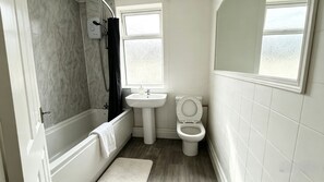 Un baño con bañera, lavamanos, inodoro y ventana.