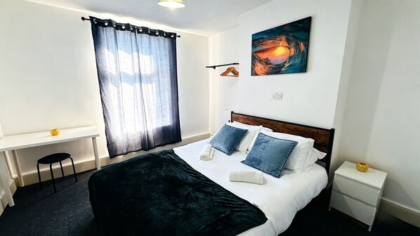 Habitación de hotel con cama, mesita de noche, escritorio, silla y un cuadro en la pared.