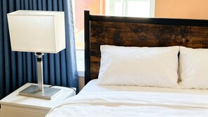 A neatly made bed with white linens, a wooden headboard, and a bedside table with a lamp. - Spacious 4BR House + Garden Retreat | Parking | 7 people (Wallasey)