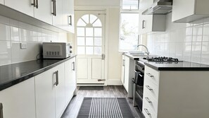 A modern kitchen with white cabinets, a microwave, a stove, and a window. - Spacious 4BR House + Garden Retreat | Parking | 7 people (Wallasey)