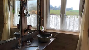Ein Badezimmer mit einem großen Spiegel, zwei Waschbecken, einem großzügigen Becken und Blick auf einen Balkon mit Geländer.