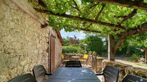 A stone building with a pergola, a table with chairs, and a small table with chairs in a garden setting.