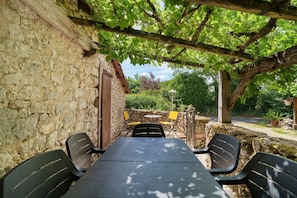 A stone building with a pergola, a table with chairs, and a small table with chairs in a garden setting.